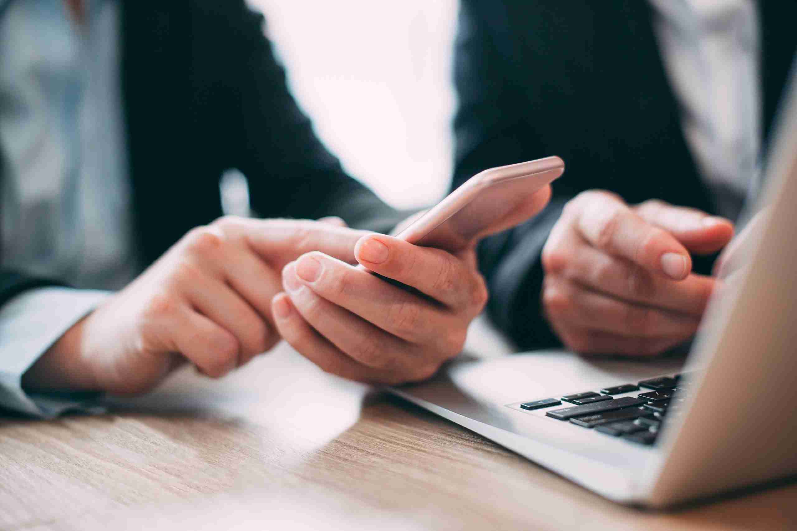 Close-up of hand of businesswoman holding mobile phone and reading message. Male colleague sitting nearby and using laptop